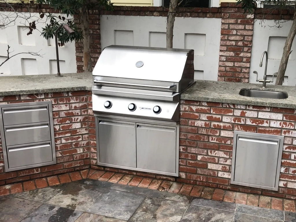 Outdoor kitchen with grill and sink in a brick patio.