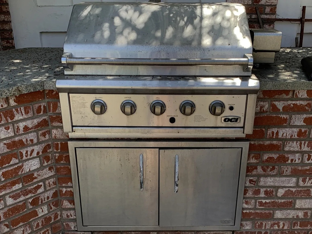 Built-in BBQ grill on brick outdoor kitchen counter.