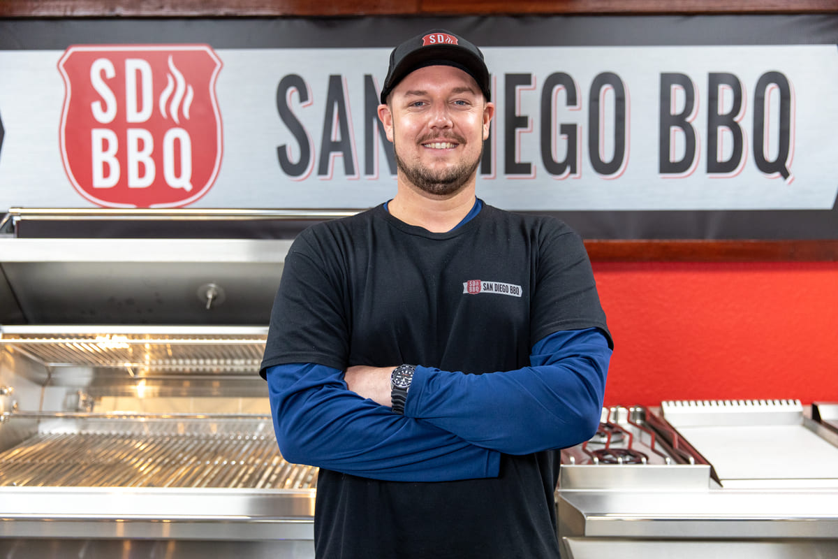 Man in BBQ showroom with company logo in background.