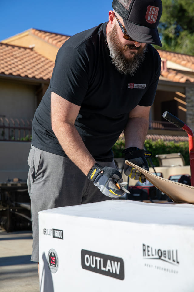 Man in black SD BBQ shirt unpacking grill equipment.