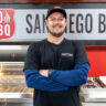 Man in BBQ showroom with company logo in background.