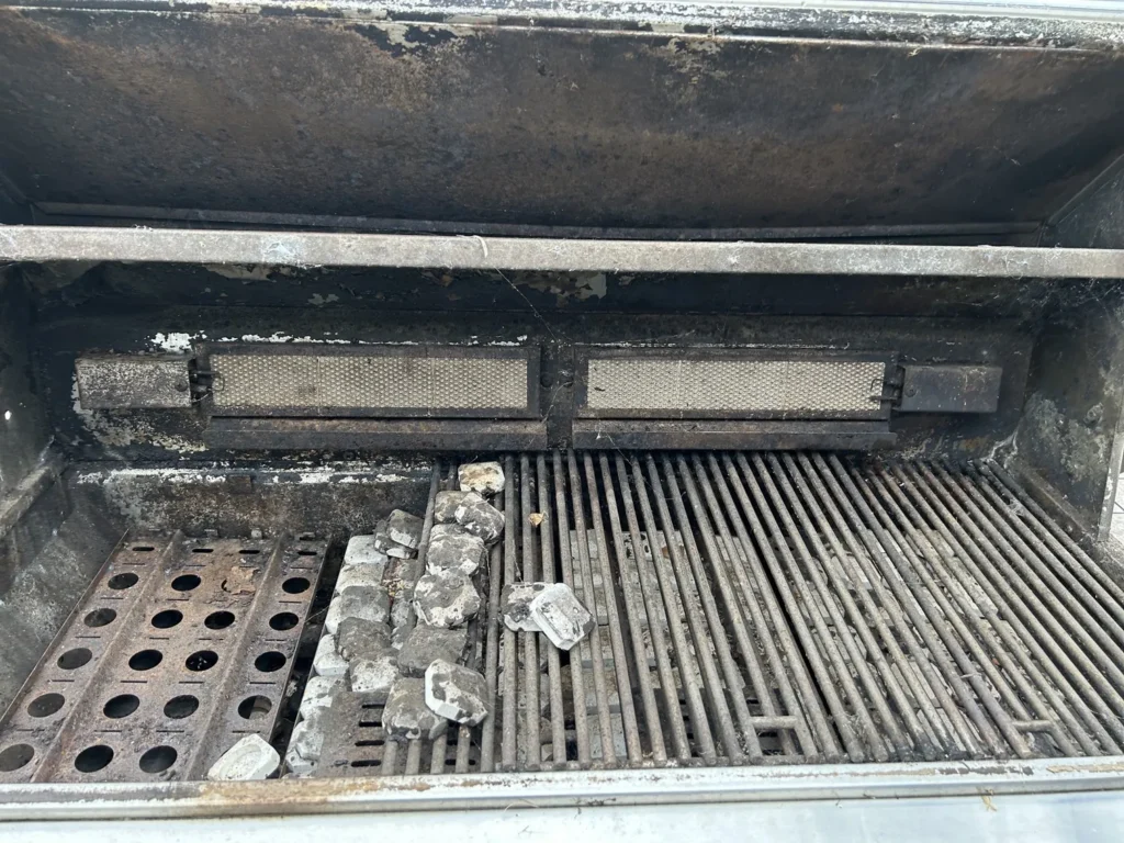 Neglected jumbo Lynx grill before cleaning, with a blackened hood, loose briquettes and grease-caked grates