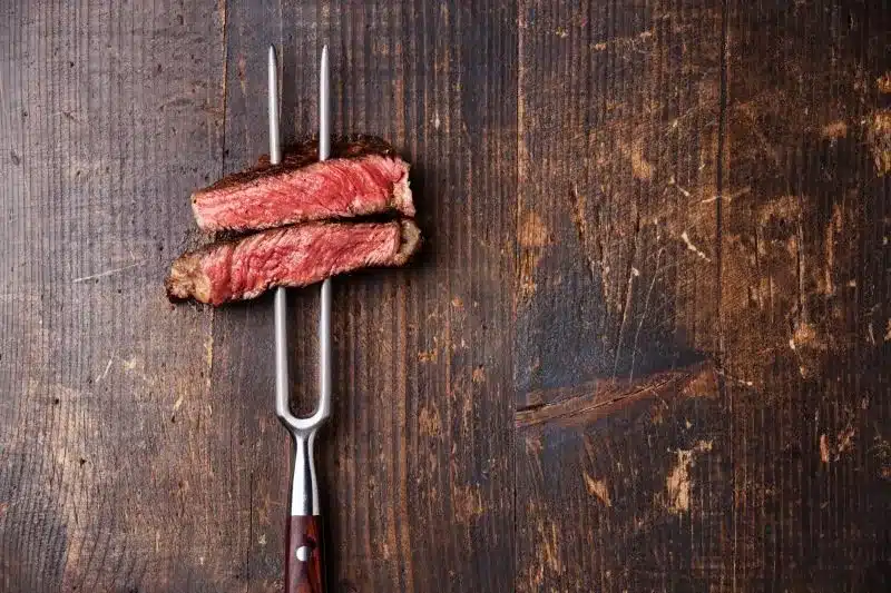 Two slices of medium-rare steak on a fork over wood
