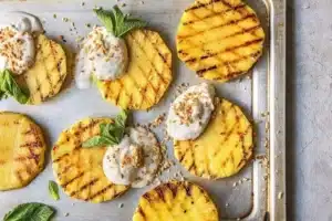Grilled pineapple slices topped with cream on baking sheet