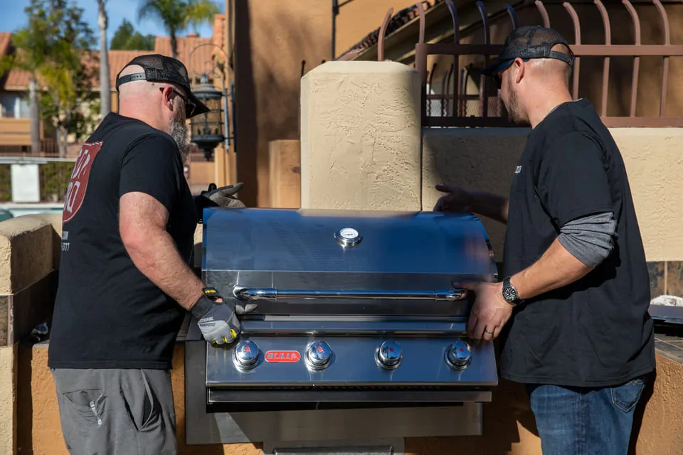 Two technicians from SDBBQ cleaning a blue grill outdoors