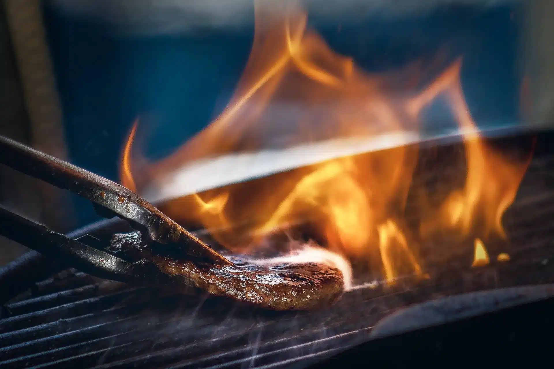Spatula flipping a steak with flames on grill