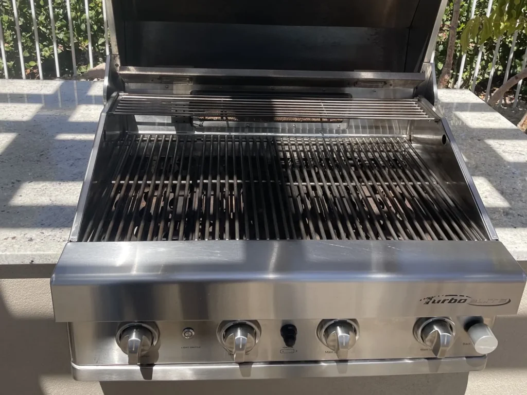 A built-in Turbo Elite gas grill with the hood open after a cleaning, its stainless steel and grates bright