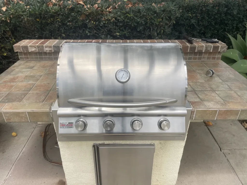 Polished Blaze four-burner built-in gas grill with the hood closed in a tiled community BBQ island