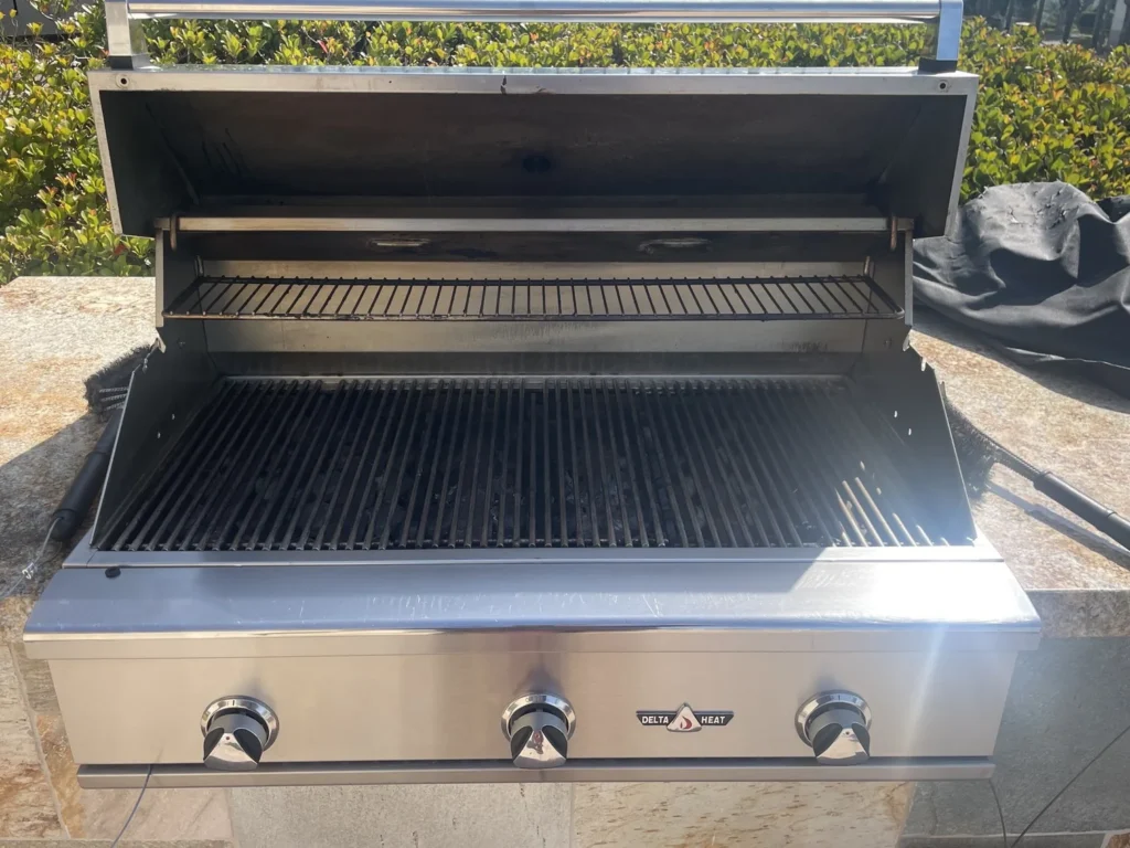 Clean Delta Heat 38-inch built-in gas grill with the hood open in a stone island by a community pool