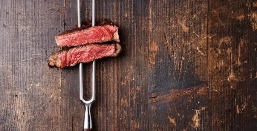 Two slices of medium-rare steak on a fork over wood