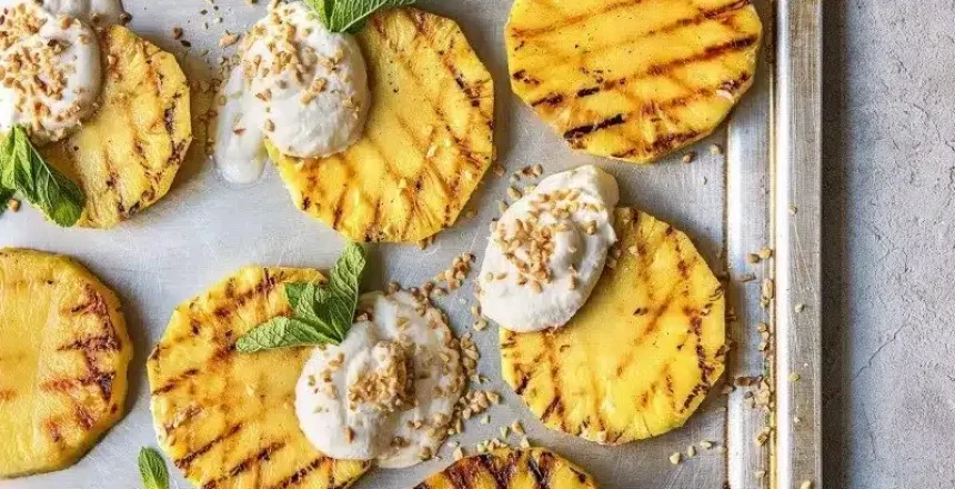 Grilled pineapple slices topped with cream on baking sheet