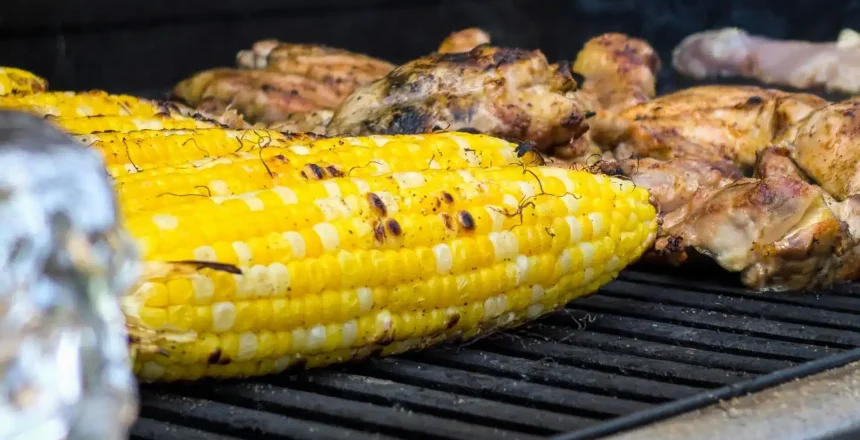 Grilling corn on the cob next to chicken